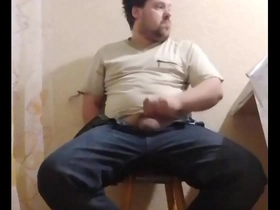 A chubby gay man sits down on a chair to pleasure himself.